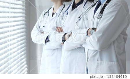 Medical team standing with arms crossed, focusing on healthcare professionals in white lab coats, representing medicine, expertise, and unity in a clinic setting 138484410