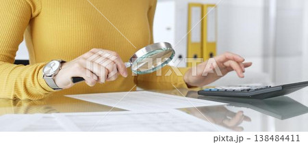 Woman doing financial paperwork, calculating budget, scrutinizing documents, and reviewing expenses with magnifying glass. Audit and taxes in business Woman doing financial paperwork, calculating budget, scrutinizing documents, and reviewing expenses with magnifying glass. Audit and taxes in business 138484411