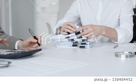 Professionals handling a large stack of documents and paperwork, signing a contract in a busy office. Audit and taxes in business Professionals handling a large stack of documents and paperwork, signing a contract in a busy office. Audit and taxes in business 138484452