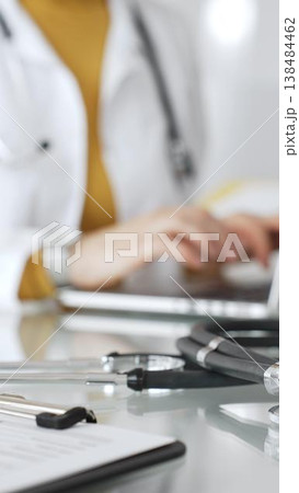 Stethoscope and clipboard with medical documents are on the table near female doctor working on laptop, managing patient data in clinic. Concept of medicine, healthcare and science Stethoscope and clipboard with medical documents are on the table near female doctor working on laptop, managing patient data in clinic. Concept of medicine, healthcare and science 138484462