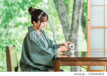 旅館の客室の縁側で日本酒を飲みながらくつろぐ浴衣羽織姿の若いアジア人女性 138484852