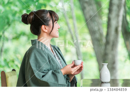 旅館の客室の縁側で日本酒を飲みながらくつろぐ浴衣羽織姿の若いアジア人女性 138484859