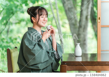 旅館の客室の縁側で日本酒を飲みながらくつろぐ浴衣羽織姿の若いアジア人女性 旅館の客室の縁側で日本酒を飲みながらくつろぐ浴衣羽織姿の若いアジア人女性 138484862