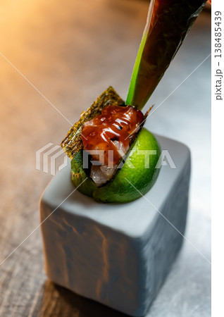 Glazed fish on lime wedge, chef piping glossy sauce over noriwrapped bite, closeup of hands and ceramic pedestal, warm spot Glazed fish on lime wedge, chef piping glossy sauce over noriwrapped bite, closeup of hands and ceramic pedestal, warm spot 138485439