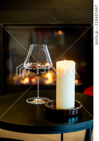 Crystal wine glass next to candle, deep reflection, warm fire glow, elegant stem, tasting pause, luxury lounge setting, 138485447