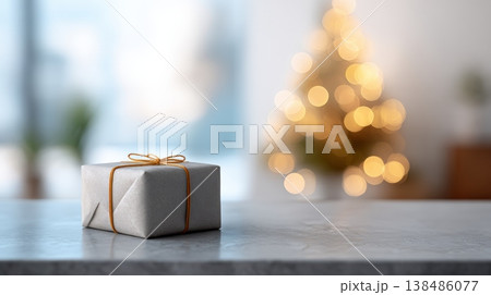 Gift box wrapped in simple paper with an orange string bow sitting on a stone surface, creating a festive holiday atmosphere with glowing bokeh lights from a christmas tree 138486077