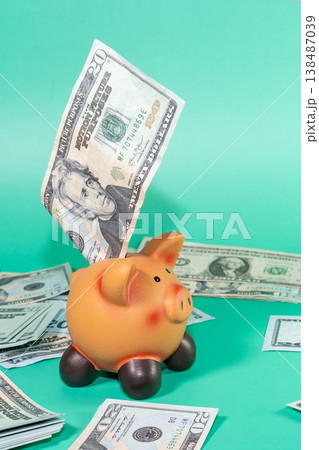 A piggy bank being filled with US currency, symbolizing savings or economic investment, with a backdrop of cash scattered around. 138487039