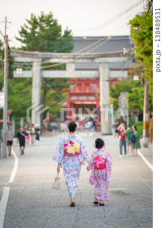 京都の神社の鳥居に向かって手をつないで歩く浴衣姿の母娘の後ろ姿。 138489531