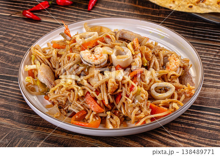 Stir-fried seafood noodles with shrimp and squid in a bowl on a wooden table. Stir-fried seafood noodles with shrimp and squid in a bowl on a wooden table. 138489771