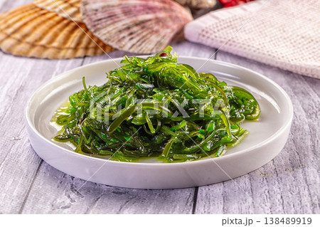Japanese seaweed salad Chuka with sesame seeds and chili in a white bowl on a wooden table. 138489919