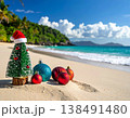 Miniature Christmas tree with santa hat and colorful ornaments on tropical beach sand with turquoise ocean and palm trees for holiday vacation and exotic celebration concepts 138491480