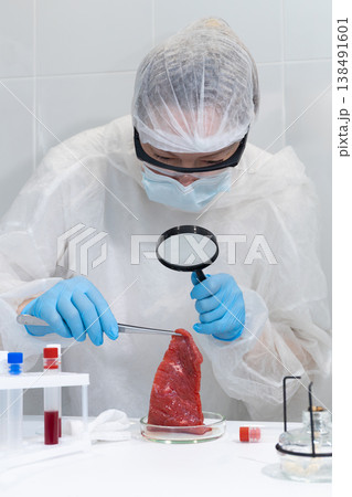 Woman scientist examining cultivated meat sample with magnifier and tweezers in lab. In vitro protein production research. Biotechnology for sustainable food and hunger solutions. photography Woman scientist examining cultivated meat sample with magnifier and tweezers in lab. In vitro protein production research. Biotechnology for sustainable food and hunger solutions. photography 138491601