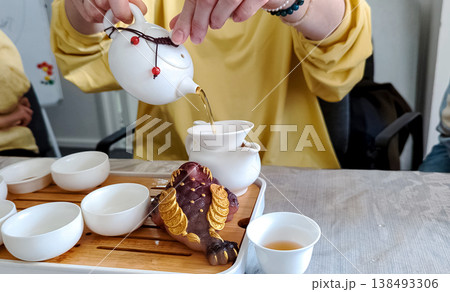 Traditional chinese tea ceremony gongfu cha with white ceramic teapot, cups and golden money frog on bamboo tray. Pouring oolong tea, mindful atmosphere, oriental culture and zen lifestyle. Traditional chinese tea ceremony gongfu cha with white ceramic teapot, cups and golden money frog on bamboo tray. Pouring oolong tea, mindful atmosphere, oriental culture and zen lifestyle. 138493306