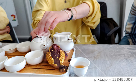 Traditional chinese tea ceremony gongfu cha with white ceramic teapot, cups and golden money frog on bamboo tray. Pouring oolong tea, mindful atmosphere, oriental culture and zen lifestyle. Traditional chinese tea ceremony gongfu cha with white ceramic teapot, cups and golden money frog on bamboo tray. Pouring oolong tea, mindful atmosphere, oriental culture and zen lifestyle. 138493307