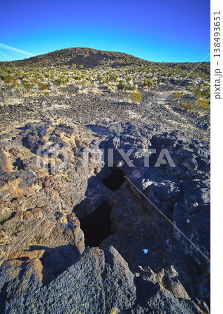 Lava Tube Entrance Volcanic Rock and Mojave Desert Landscape Under Blue Sky Lava Tube Entrance Volcanic Rock and Mojave Desert Landscape Under Blue Sky 138493651