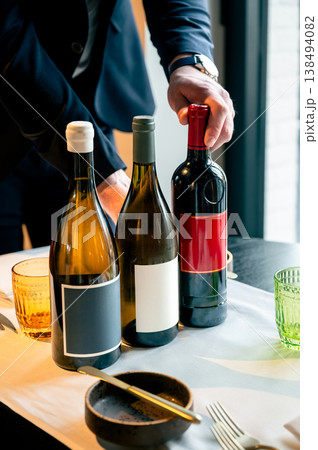 Wine service scene. Expert sommelier carefully uncorks bottle for guests at upscale restaurant Wine service scene. Expert sommelier carefully uncorks bottle for guests at upscale restaurant 138494082