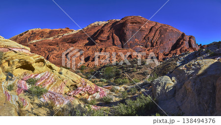 Red Sandstone Cliffs Colorful Banded Rocks and Desert Vegetation Under Blue Sky 138494376