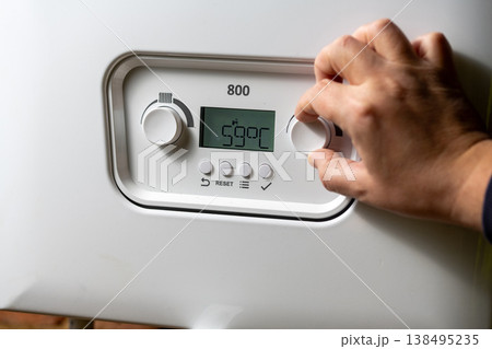 Men hand setting temperature button on control panel of central heating at combi boiler. Incressing price for gas Men hand setting temperature button on control panel of central heating at combi boiler. Incressing price for gas 138495235