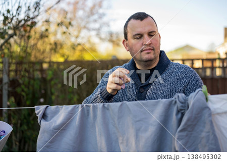 Man hangs up laundry to dry outdoors on hanging rope. Father performs home duties. 138495302