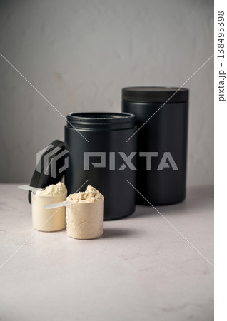Protein powder in scoops with black protein tubes, jars in background. Body building, muscle growth and food supplement concept Protein powder in scoops with black protein tubes, jars in background. Body building, muscle growth and food supplement concept 138495398