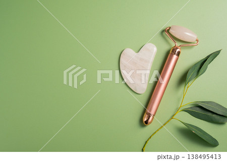 Gua sha tool and face massage roller on green background, beauty abstract photo. Top view. Gua sha tool and face massage roller on green background, beauty abstract photo. Top view. 138495413