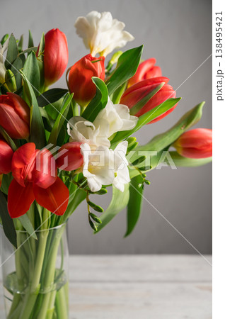 Spring floral background. Red tulips and Fresia white flower bouquet in glass vase. Copy space 138495421