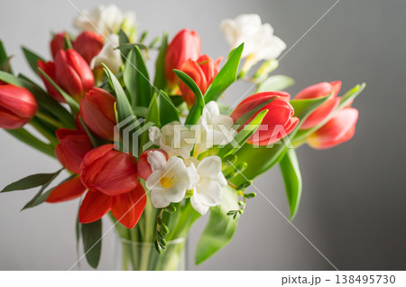 Spring floral background. Red tulips and Fresia white flower bouquet in glass vase. Copy space 138495730
