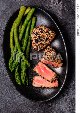Tuna steak fried in sesame seeds served with asparagus. 138498317