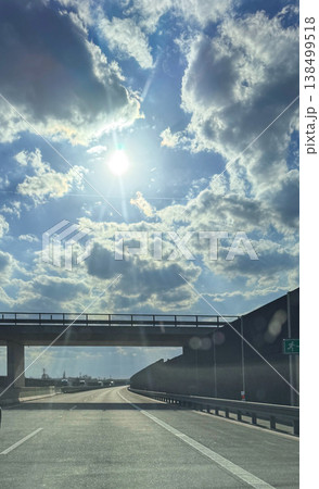 Highway road under overpass with dramatic clouds and bright sun rays in blue sky for transport travel scene Highway road under overpass with dramatic clouds and bright sun rays in blue sky for transport travel scene 138499518