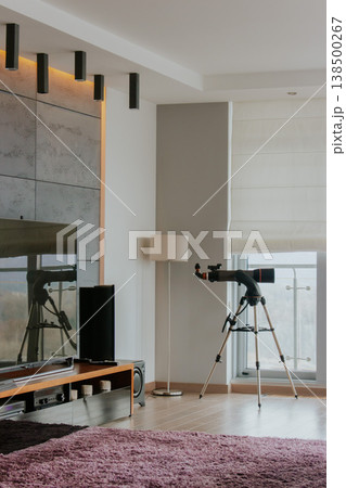 Cozy modern apartment concept. Luxury interior design. Telescope in modern apartment. Dream house decoration. TV set and domestic telescope near the window. Atmospheric living room design. 138500267