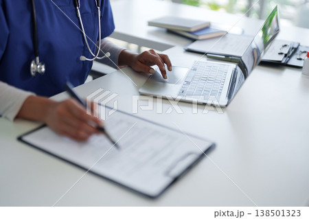 Adult medical professional working at hospital office desk managing patient data documents healthcare administration nurse doctor physician writing records Adult medical professional working at hospital office desk managing patient data documents healthcare administration nurse doctor physician writing records 138501323