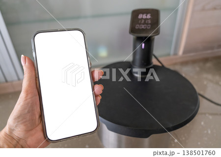 Smartphone controlling sous vide circulator on kitchen counter modern cooking technology Smartphone controlling sous vide circulator on kitchen counter modern cooking technology 138501760