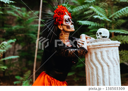 Day of the Dead. Profile portrait of a woman with a wreath of red roses and a skull on a column. Artistic composition Day of the Dead. Profile portrait of a woman with a wreath of red roses and a skull on a column. Artistic composition 138503309