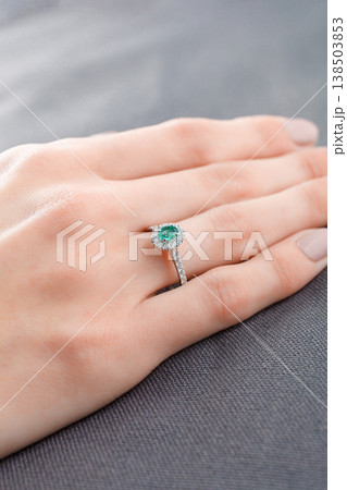 Beautiful female hand with gold ring with diamonds and emerald on gray background Beautiful female hand with gold ring with diamonds and emerald on gray background 138503853