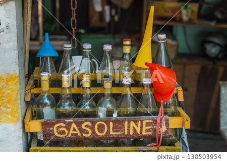 Local roadside gasoline sold in glass bottles with funnels in tropical workshop on Koh Samui, informal fuel retail concept in Southeast Asia Local roadside gasoline sold in glass bottles with funnels in tropical workshop on Koh Samui, informal fuel retail concept in Southeast Asia 138503954