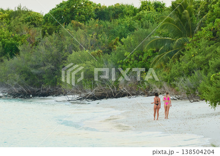 A beautiful tanned girls in a swimsuit walking along the white beach at sunset in the Maldives, they are happy, posing for a photographer A beautiful tanned girls in a swimsuit walking along the white beach at sunset in the Maldives, they are happy, posing for a photographer 138504204