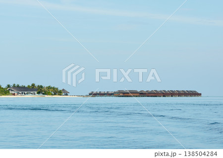 Classic Maldives island landscape on a sunny day, coastal luxury resort buildings, azure water, white sand, palm trees on the shore 138504284