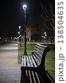 Empty park bench resting beside a paved pathway with modern streetlights creating a peaceful ambiance, offering a quiet space for contemplation or relaxation outdoors 138504635