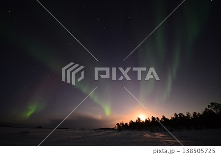 フィンランドのラップランド地方イナリにて、雪景色のコテージの上に現れた幻想的な緑のオーロラ。 138505725