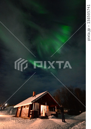 フィンランドのラップランド地方イナリにて、雪景色のコテージの上に現れた幻想的な緑のオーロラ。 138505741
