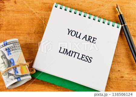 A motivational note reading You are limitless rests atop a wooden surface beside a rolled-up bill and a sleek pen, inspiring thoughts of prosperity A motivational note reading You are limitless rests atop a wooden surface beside a rolled-up bill and a sleek pen, inspiring thoughts of prosperity 138506124