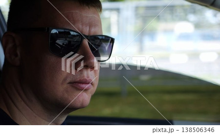 Profile of confident man driving a motor car at town. Male face of male driver in sunglasses looking concentrated to urban road while riding automobile. Slow motion Profile of confident man driving a motor car at town. Male face of male driver in sunglasses looking concentrated to urban road while riding automobile. Slow motion 138506346