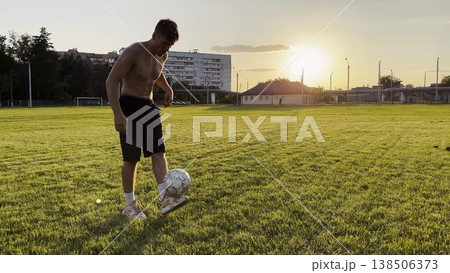 Young man juggling soccer ball on stadium at sunset. Professional footballer kicking ball at green field. Sportsman practicing tricks at meadow with sunlight at background. Freestyle football Young man juggling soccer ball on stadium at sunset. Professional footballer kicking ball at green field. Sportsman practicing tricks at meadow with sunlight at background. Freestyle football 138506373