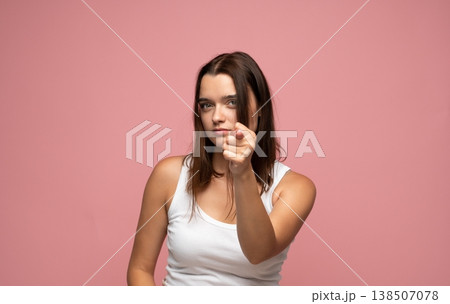 Young woman pointing directly at camera with serious, confident expression on pink background, indicating choice or accusation Young woman pointing directly at camera with serious, confident expression on pink background, indicating choice or accusation 138507078