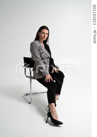 Woman wearing a stylish two-tone blazer and black trousers, sitting confidently on a modern chair in a studio, representing business, fashion, and corporate success Woman wearing a stylish two-tone blazer and black trousers, sitting confidently on a modern chair in a studio, representing business, fashion, and corporate success 138507108