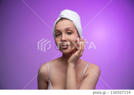 Young woman applying face cream, pampering facial skin, moisturizing after showering for wellness and beauty, embracing self care against a purple background Young woman applying face cream, pampering facial skin, moisturizing after showering for wellness and beauty, embracing self care against a purple background 138507154