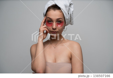 Young woman completing beauty routine, applying under eye patches, wearing a towel on her hair for refreshing skincare, feeling calm and practicing self-care at home Young woman completing beauty routine, applying under eye patches, wearing a towel on her hair for refreshing skincare, feeling calm and practicing self-care at home 138507166