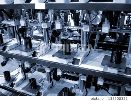Many 3D printers printing object. 3D printers creating shape from molten plastic flowing out of extruder. 3D printer close up. Working 3D printer in process printing object from molten black plastic Many 3D printers printing object. 3D printers creating shape from molten plastic flowing out of extruder. 3D printer close up. Working 3D printer in process printing object from molten black plastic 138508321
