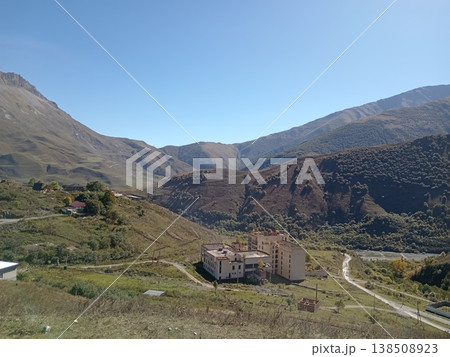 Top view of a mountain village in the Caucasus Mountains, North Ossetia, Russia. Overhead perspective of traditional houses clustered in a green valley surrounded by peaks Top view of a mountain village in the Caucasus Mountains, North Ossetia, Russia. Overhead perspective of traditional houses clustered in a green valley surrounded by peaks 138508923