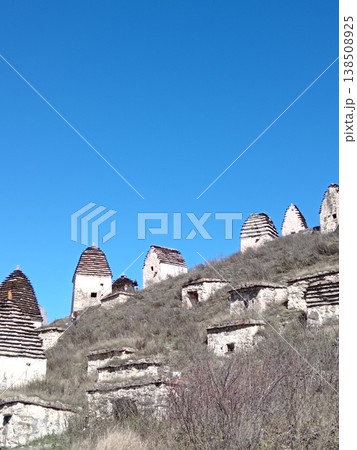 View of the City of the Dead, Dargavs necropolis, North Ossetia, Russia. Ancient stone crypts scattered across a green mountain slope under a blue sky View of the City of the Dead, Dargavs necropolis, North Ossetia, Russia. Ancient stone crypts scattered across a green mountain slope under a blue sky 138508925